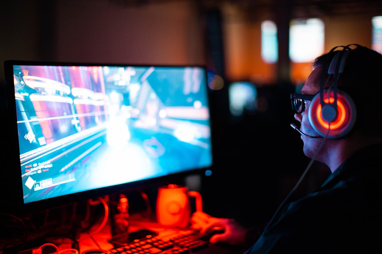 PC gamer wearing illuminated headphones playing a first-person shooter in a dark room with RGB lighting